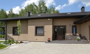 Elewacja domu w kolorze kawa z mlekiem, z kamiennymi elementami i zielenią.