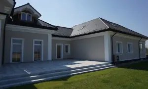Nowoczesny dom z tarasem i trawnikiem. Elegancki gzyms podkreśla architekturę budynku.