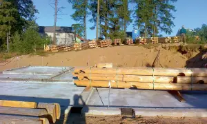 Drewniane bale przygotowane do budowy domu na betonowym fundamencie.