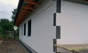 Nowy dom z białym ociepleniem styropianowym. Elewacja domu w trakcie budowy, widoczne okna i fragment dachu.