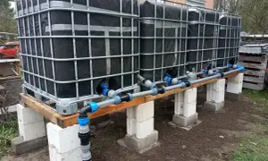 Kilka połączonych zbiorników IBC na drewnianej konstrukcji z systemem rur i zaworów.