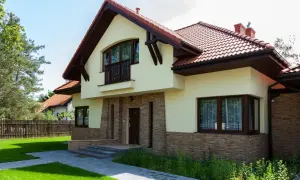 Nowoczesny dom z kamienną okładziną i drewnianymi elementami. Przestronna kubatura budynku podkreślona przez duże okna i balkon.