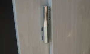Metalowy zawias na jasnych drzwiach. Dowiedz się, jak podnieść drzwi na zawiasach, aby je wyregulować lub zdjąć.