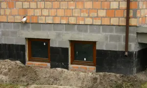 Fundament domu z oknami piwnicznymi, izolacją przeciwwilgociową i ceglanym murem.