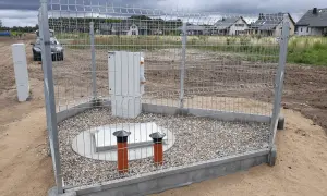 Nowa przepompownia ścieków w otoczeniu domów jednorodzinnych, zabezpieczona ogrodzeniem.