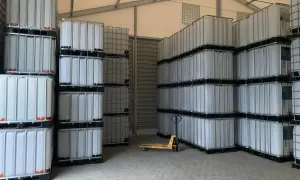 Magazyn pełen białych mauzerów 1000l, ułożonych w stosy. Widać wózek paletowy.
