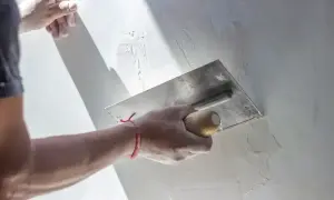 Ręka z kielnią nakłada tynk kornik na ścianę, tworząc charakterystyczną fakturę.