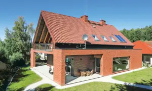 Nowoczesny dom z czerwonej cegły i czerwonym dachem dwuspadowym, z balkonem i oknami dachowymi.
