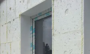 Fragment elewacji z białego styropianu z widocznym oknem i pianką montażową.