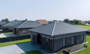 Nowoczesne domy z szarymi dachami z blachy, otoczone zielenią i podjazdami.