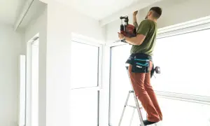 Mężczyzna na drabinie montuje szynę sufitową, dbając o odpowiednią odległość od ściany.