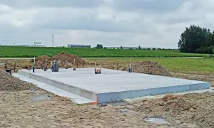 Płyta fundamentowa koszt budowy domu. Betonowa płyta na placu budowy, otoczona piaskiem i zielenią.