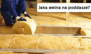 Ocieplanie poddasza wełną mineralną. Pracownik układa rolkę izolacji między drewnianymi belkami.
