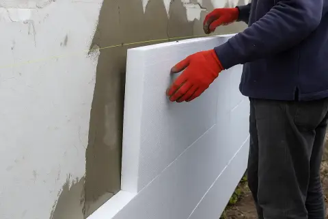 Układanie styropianu na ścianie. Siatka i klej czekają, by obniżyć cenę robocizny.