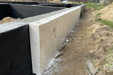 Izolacja fundamentów styropianem na czarnej ścianie fundamentowej.