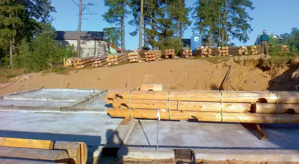 Drewniane bale przygotowane do budowy domu na betonowym fundamencie.