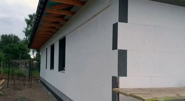 Nowy dom z białym ociepleniem styropianowym. Elewacja domu w trakcie budowy, widoczne okna i fragment dachu.