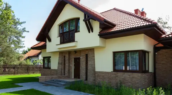Nowoczesny dom z kamienną okładziną i drewnianymi elementami. Przestronna kubatura budynku podkreślona przez duże okna i balkon.