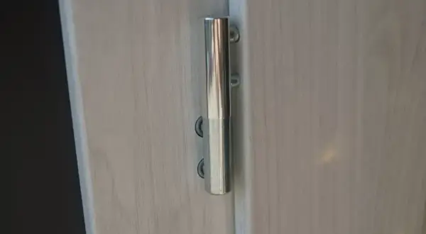 Metalowy zawias na jasnych drzwiach. Dowiedz się, jak podnieść drzwi na zawiasach, aby je wyregulować lub zdjąć.