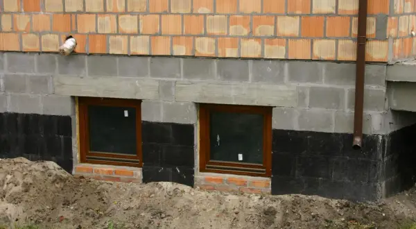 Fundament domu z oknami piwnicznymi, izolacją przeciwwilgociową i ceglanym murem.