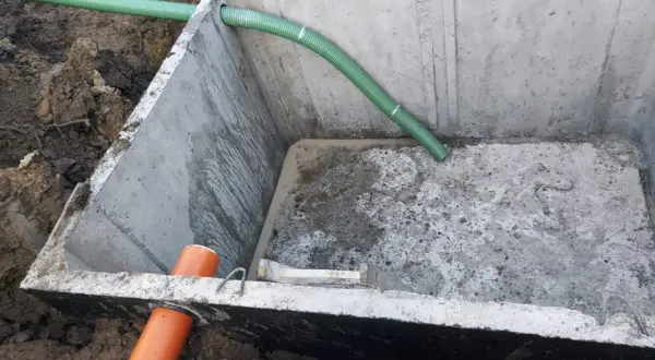 Szambo betonowe 10m3 cena z montażem. Instalacja wkopana w ziemię, widoczne rury doprowadzające.