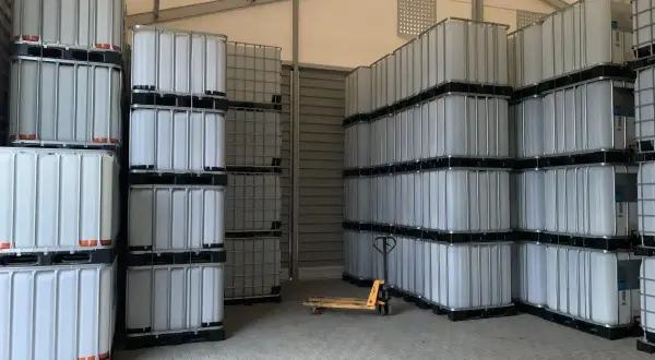 Magazyn pełen białych mauzerów 1000l, ułożonych w stosy. Widać wózek paletowy.