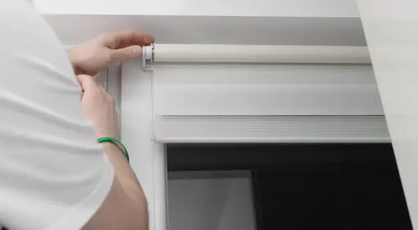 Dłoń naprawia mechanizm rolety dzień-noc.