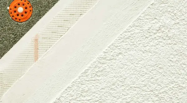 Warstwy tynku mineralnego na elewacji: styropian, siatka, tynk bazowy i wykończeniowy.