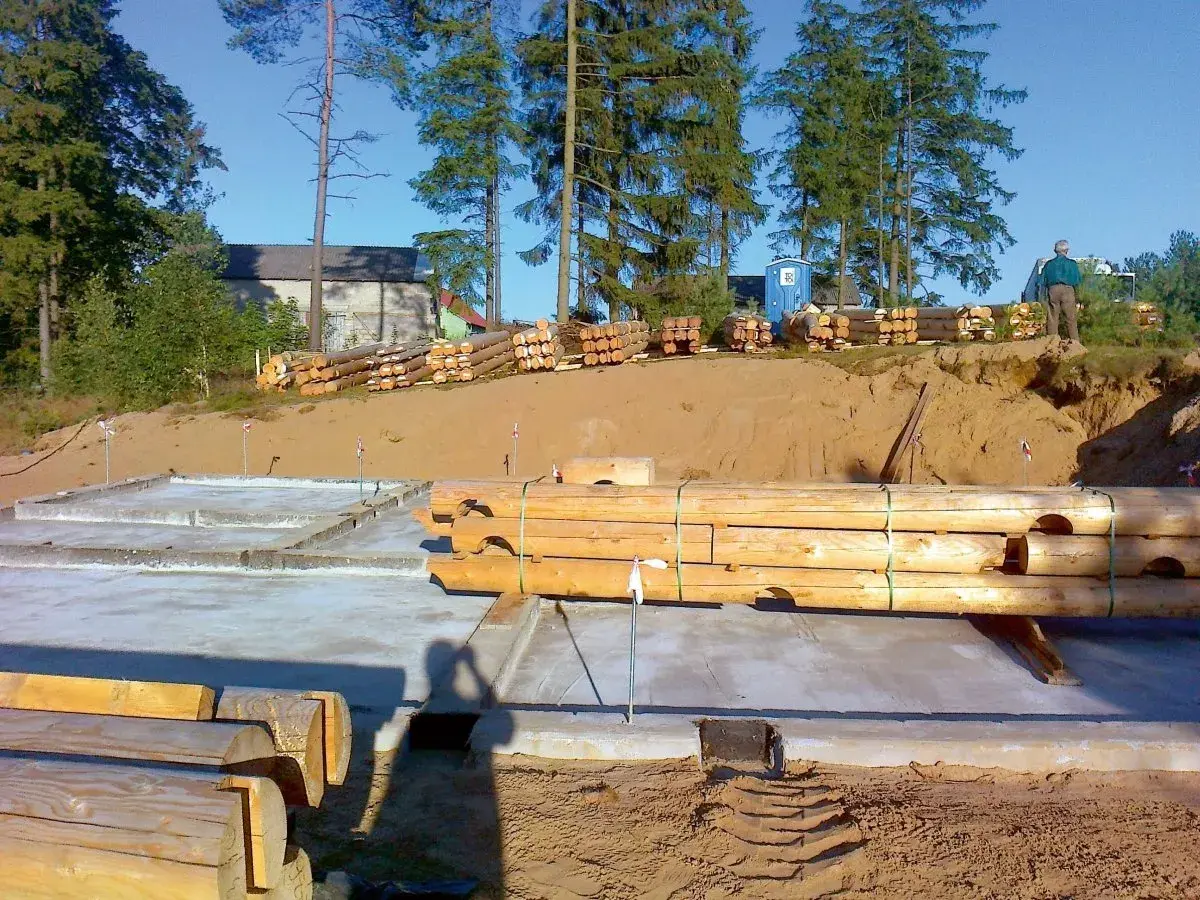 Drewniane bale przygotowane do budowy domu na betonowym fundamencie.