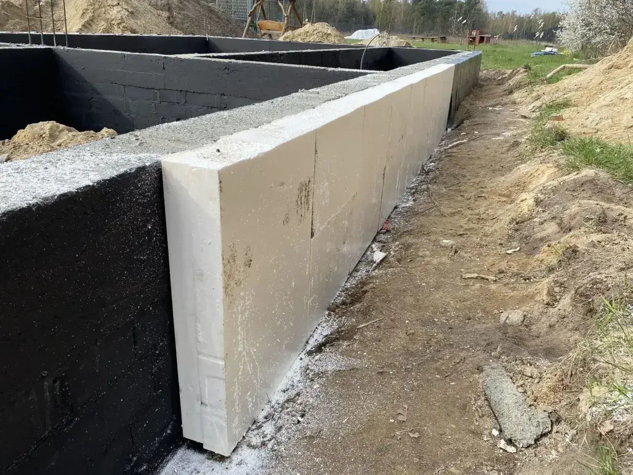 Izolacja fundamentów styropianem na czarnej ścianie fundamentowej.