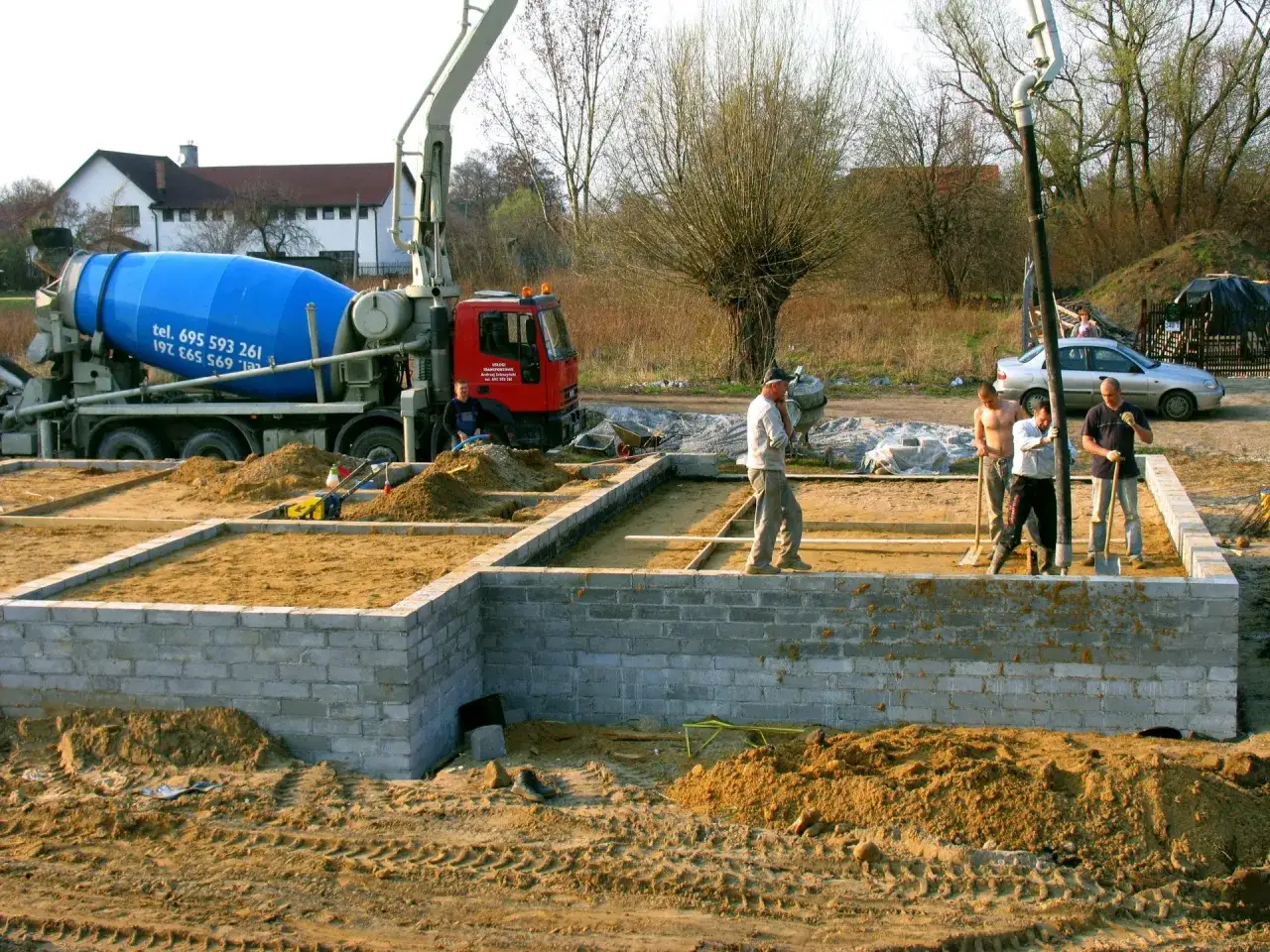 Budowa fundamentów: betoniarka, koparka i pracownicy zastanawiają się, ile waży metr sześcienny piasku.