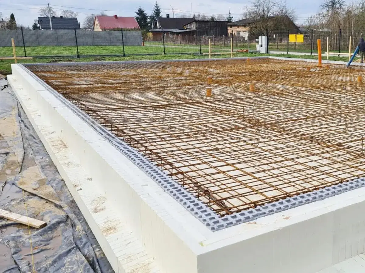 Fundament zbrojony pod zalewanie betonem. Widać styropianowe szalunki tracone i siatkę zbrojeniową.