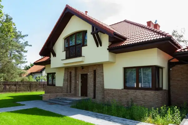 Nowoczesny dom z kamienną okładziną i drewnianymi elementami. Przestronna kubatura budynku podkreślona przez duże okna i balkon.