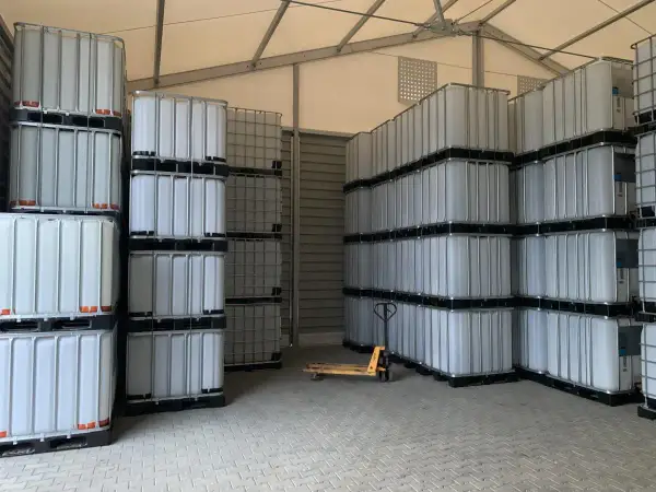 Magazyn pełen białych mauzerów 1000l, ułożonych w stosy. Widać wózek paletowy.
