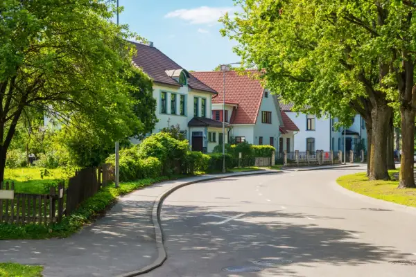 Ulica z domami i drzewami. Szerokość drogi dojazdowej pozwala na swobodny ruch.
